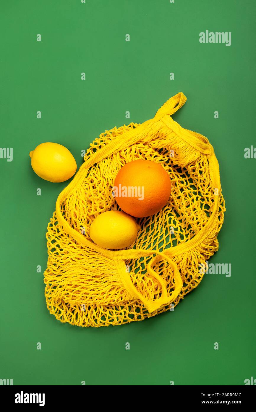 Fruit Lemons And Orange In Yellow String Mesh Reusable Bag On The Green