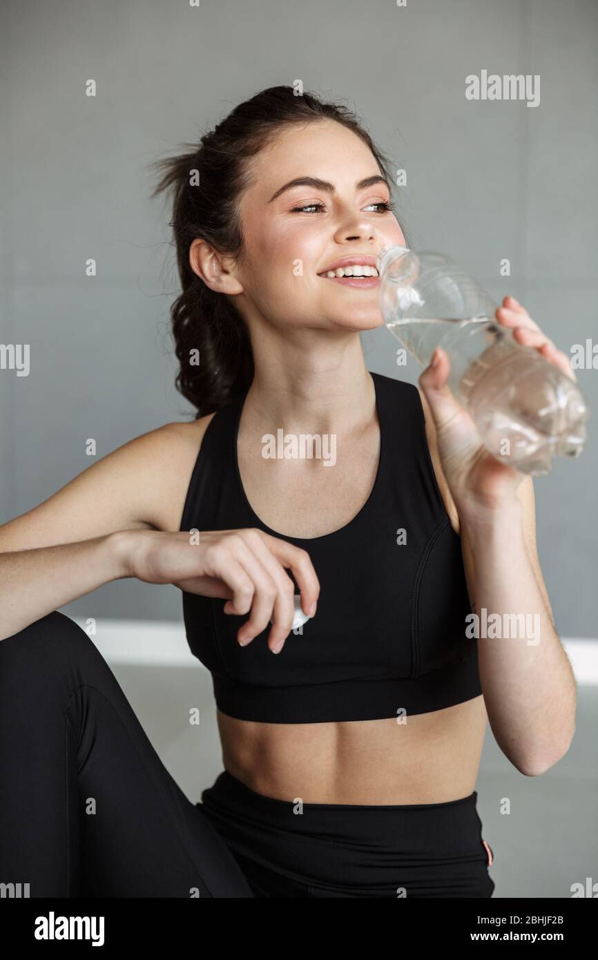 Photo Of Pleased Brunette Woman In Sportswear Drinking Water And