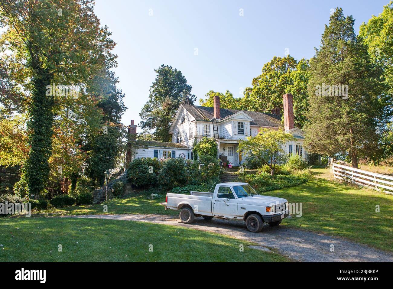 A Beat Up Pickup Truck Sits Parked In Front Of A White Farmhouse