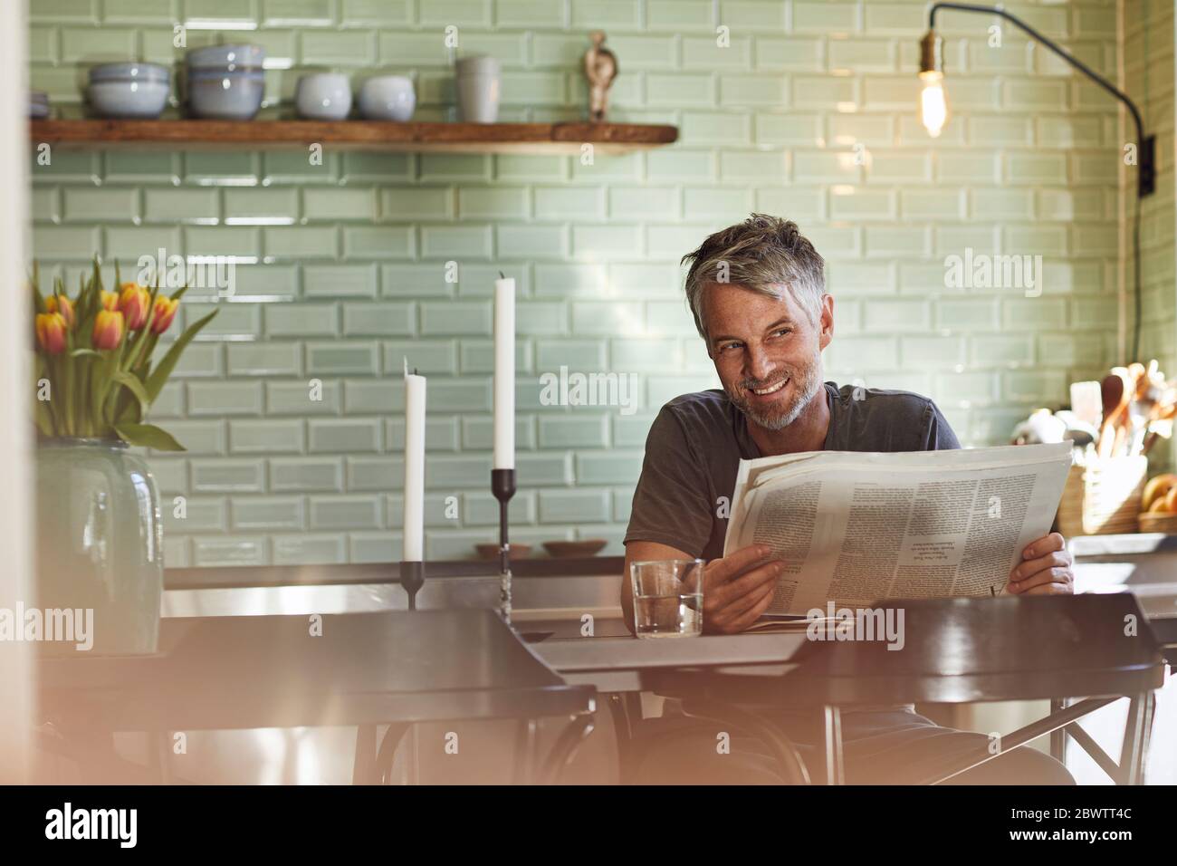 Smiling Mature Man Sitting In Kitchen Reading Newspaper Stock Photo Alamy