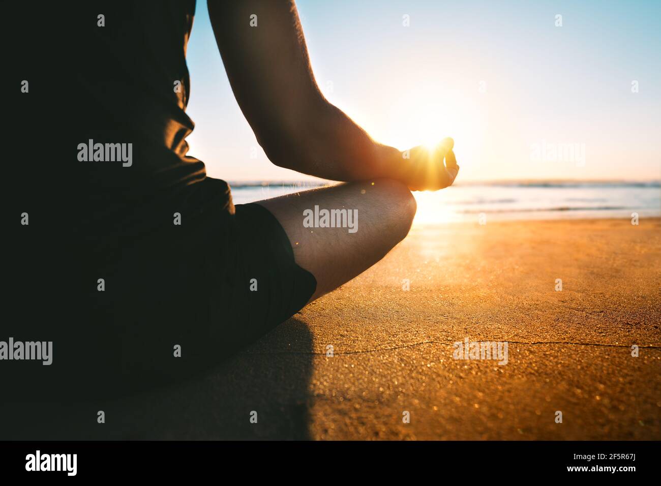 Man Meditates On The Beach At Sunset Or Sunrise Sitting On The Sand In