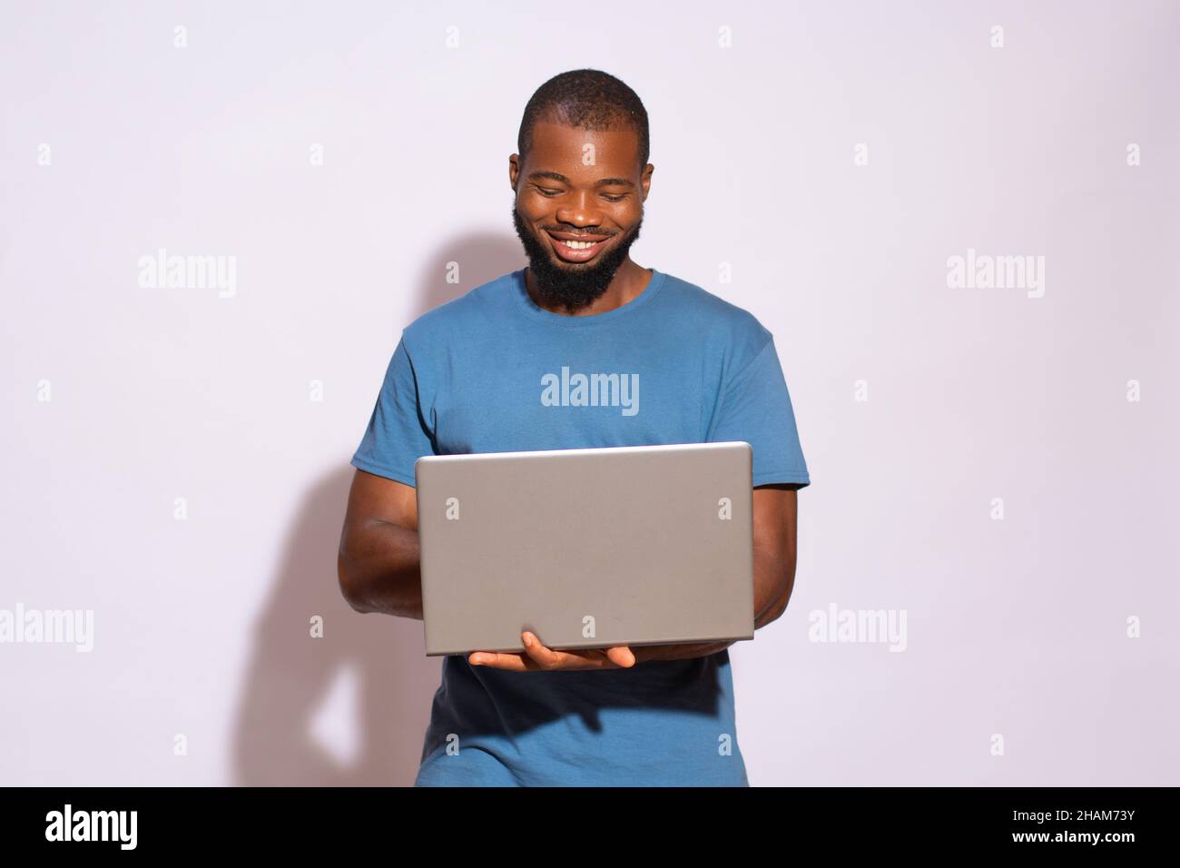 Black Man With A Blue T Shirt Smiling Holding A Laptop In His Hands On