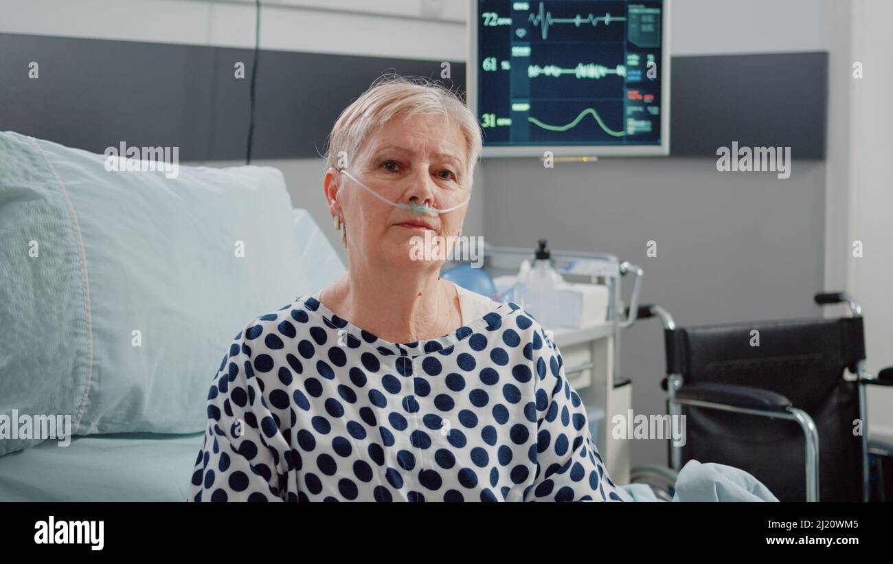 Portrait Of Sick Patient Sitting In Hospital Ward Bed With Nasal Oxygen