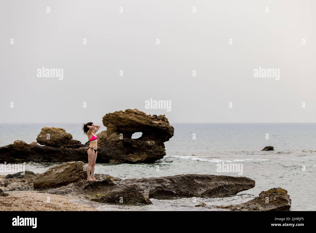 A Caucasian Woman In A Bikini Standing On The Rocks Of A Beach And