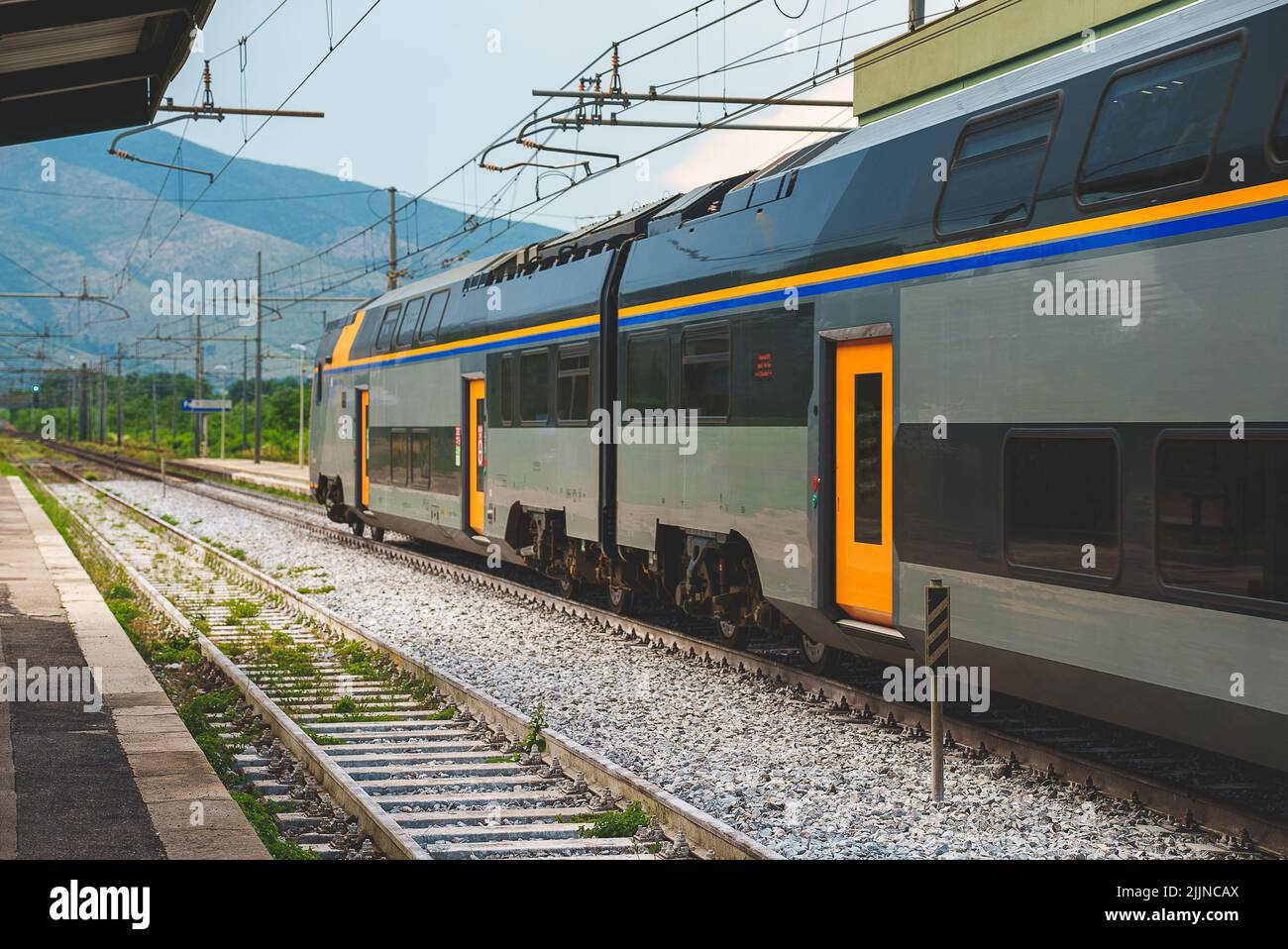 Double Decker Train Passing By The Train Station In Italy Stock Photo