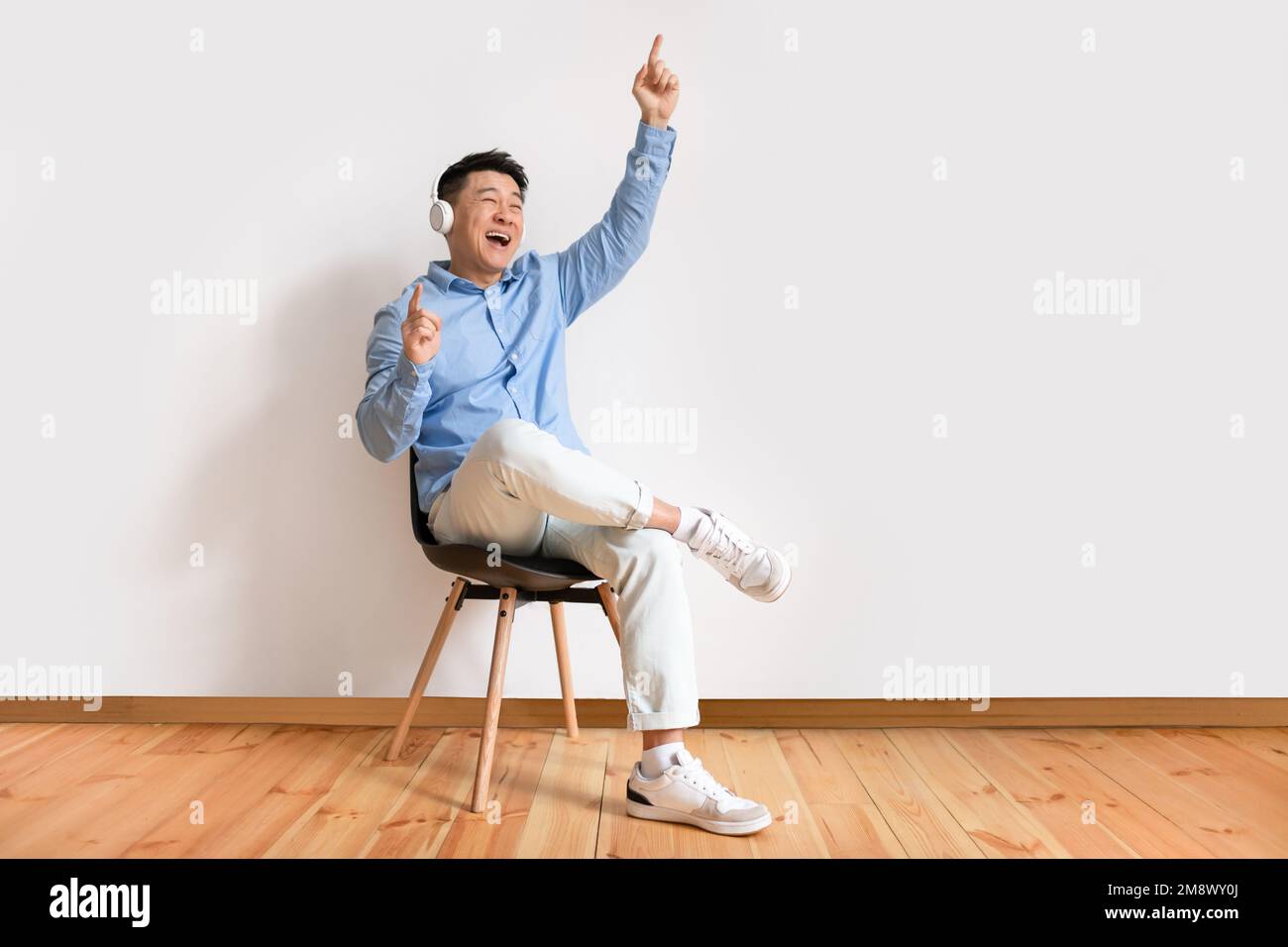 Joyful Asian Mature Man In Wireless Headphones Sitting On Chair And