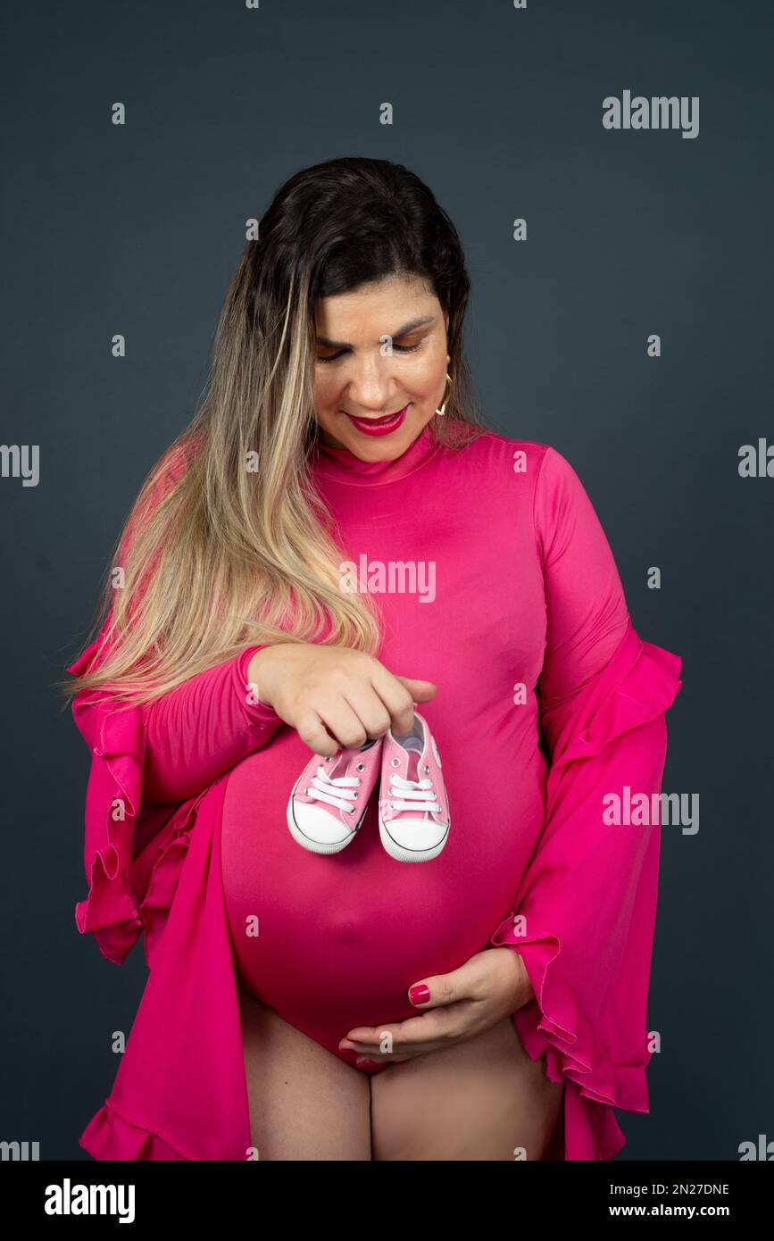 Pregnant Woman Standing Holding Baby Shoes Over Her Belly Isolated