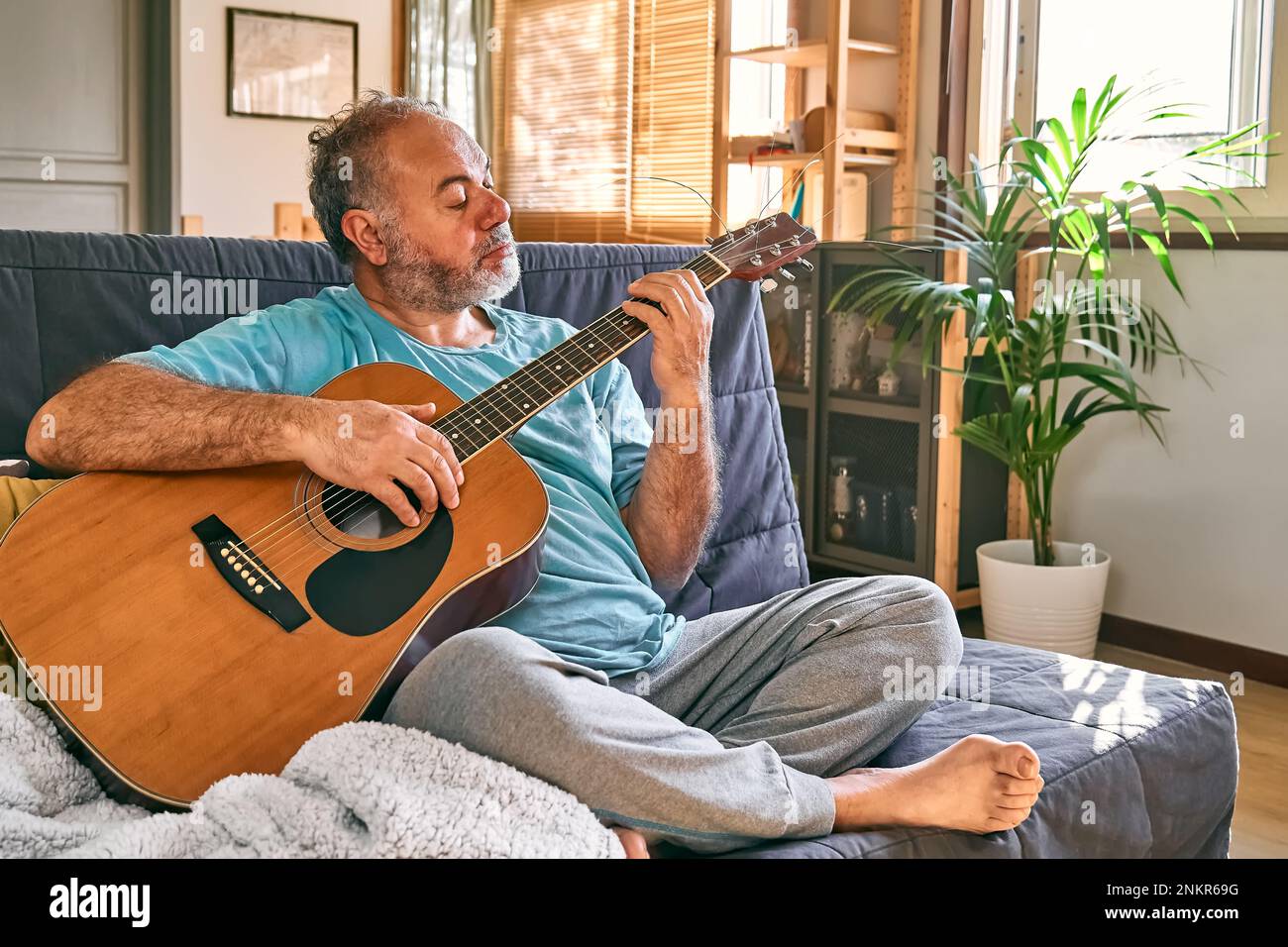 Middle Aged Bearded Man Playing Acoustic Guitar While Sitting On Sofa