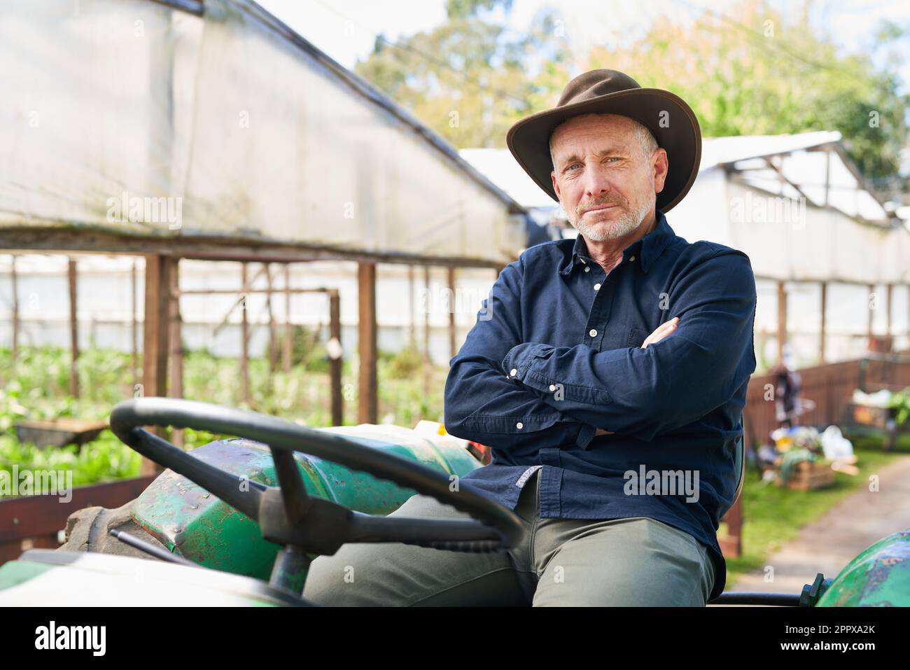 Portrait Of Confident Mature Farmer Sitting With Arms Crossed On