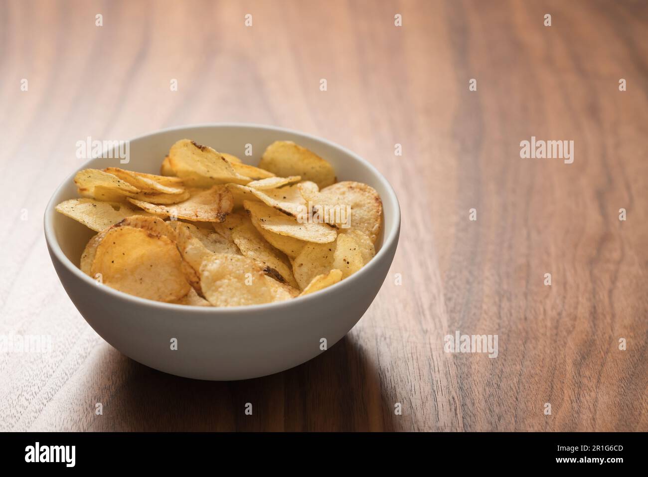 Organic Potato Chips With Black Pepper In White Ceramic Bowl On Walnut