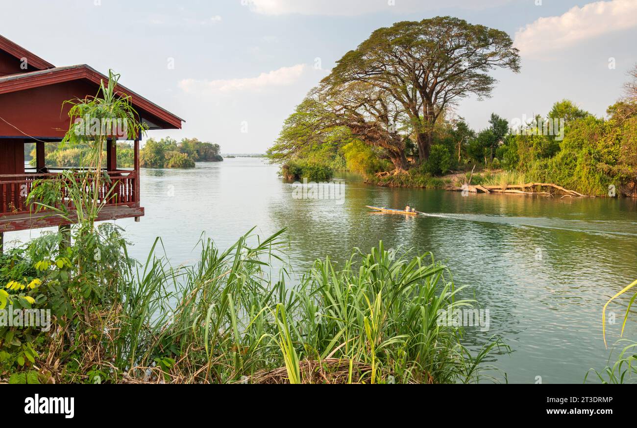 River Boat Heading Upstream Close To Sunset Traditional Laotian Hut On