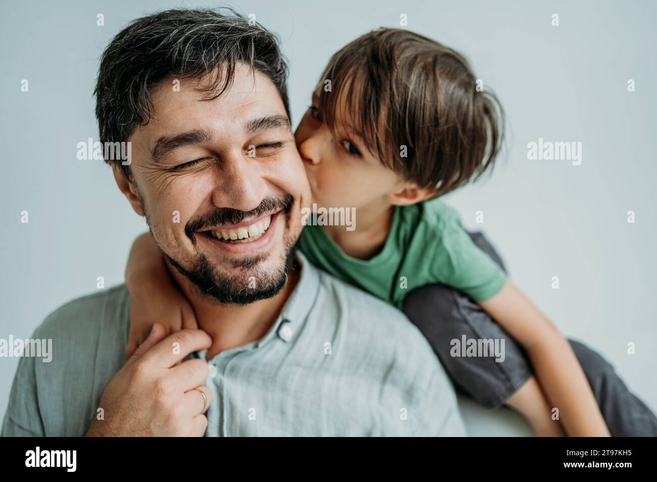 Son Kissing Happy Father On Cheeks Against White Background Stock Photo