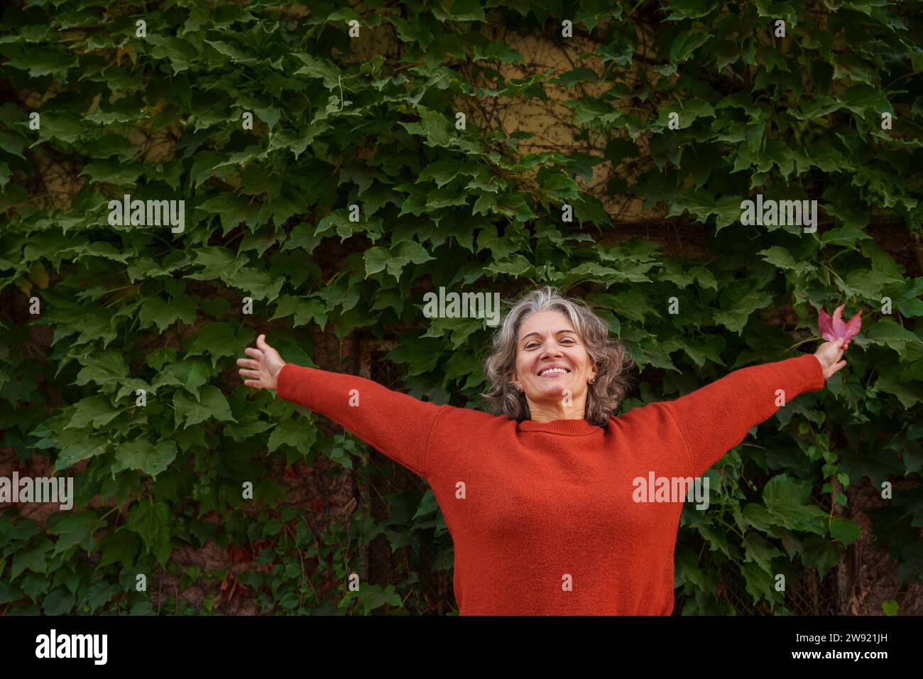 Happy Mature Woman With Arms Outstretched In Front Of Plants Stock