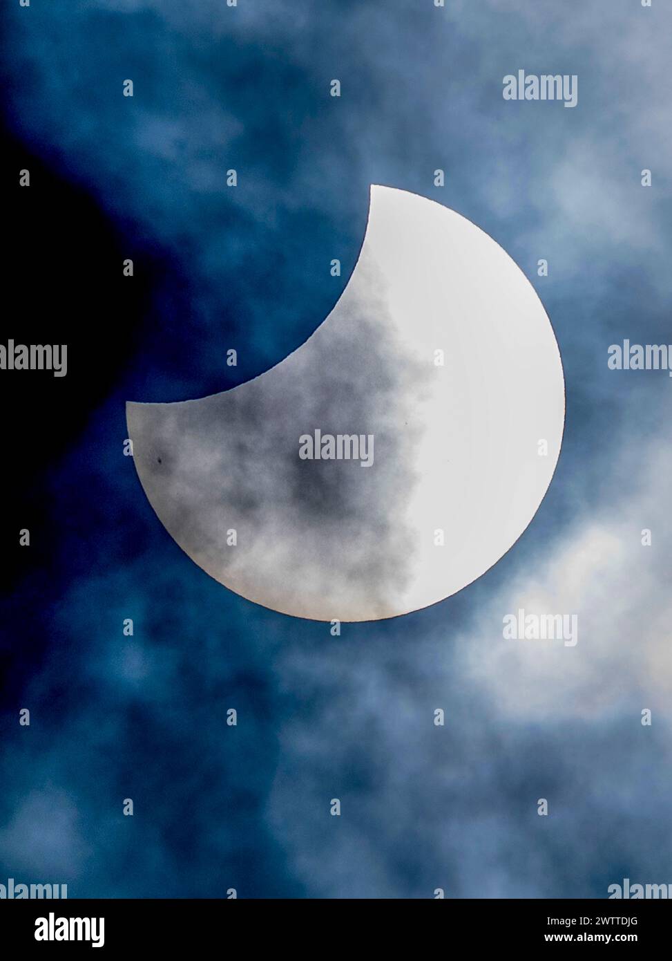 A Partial Solar Eclipse Veiled By Wispy Clouds Against A Deep Blue Sky