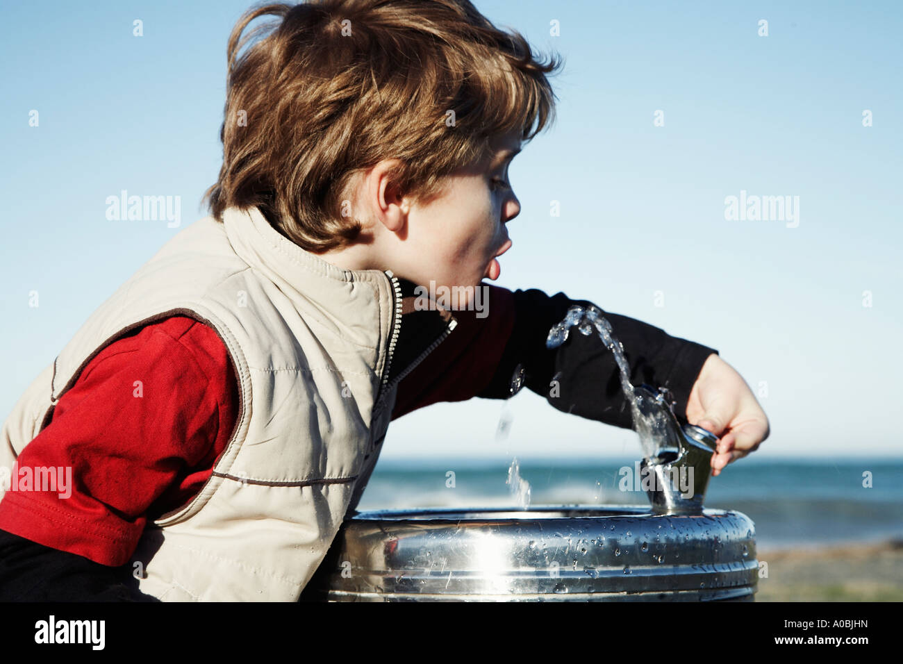 young-boy-drinking-from-water-fountain-bubbler-with-blue-sky-behind-A0BJHN.jpg