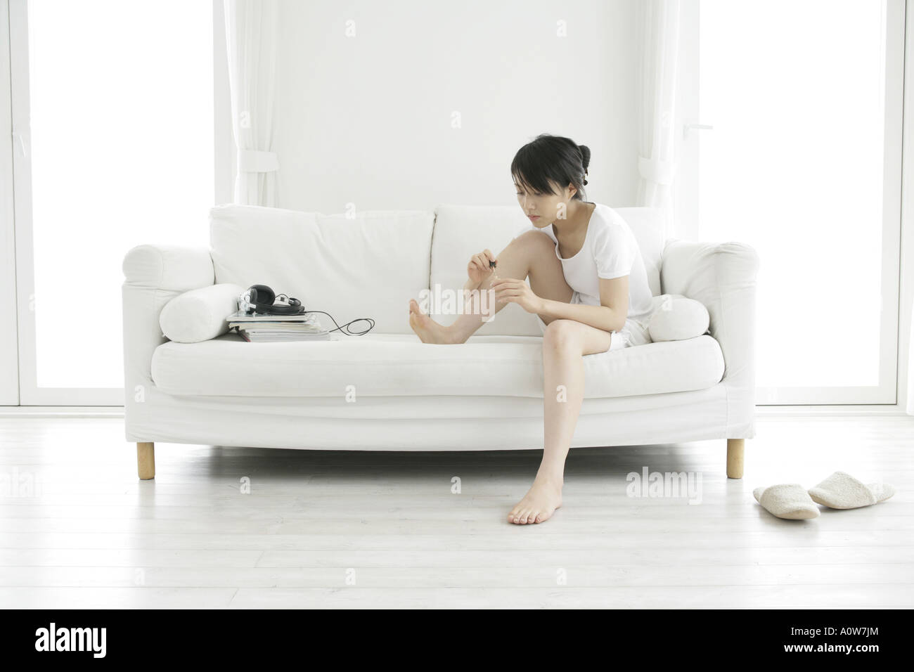 Young Woman Sitting On A Couch And Applying Nail Polish Stock