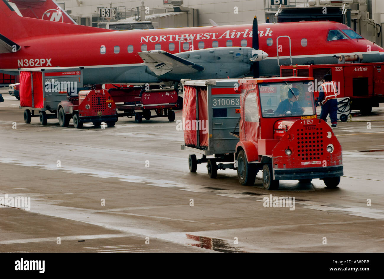 Airport baggage handler driving a baggage truck past an aircraft Stock