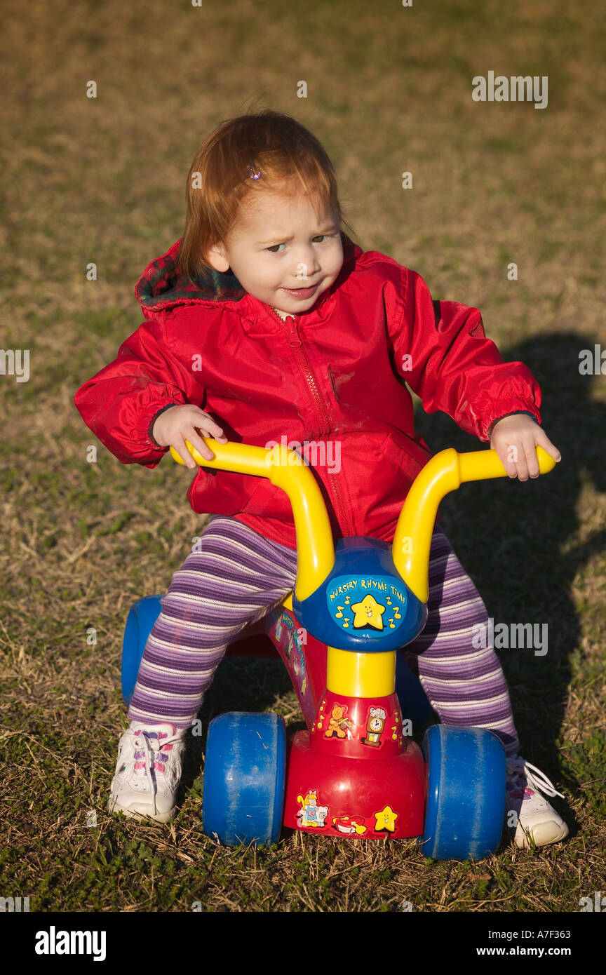 Two Year Old Girl In Red Coat Riding Plastic Trike On Lawn Stock ...
