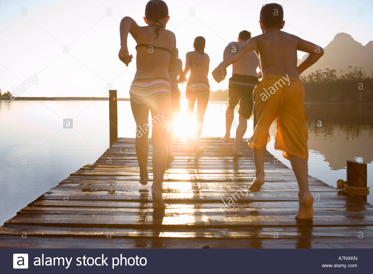 Kids Swimming In A Lake family in swimwear running along jetty jumping into lake at sunset Kids Swimming In A Lake family in swimwear running along jetty jumping into lake at sunset
