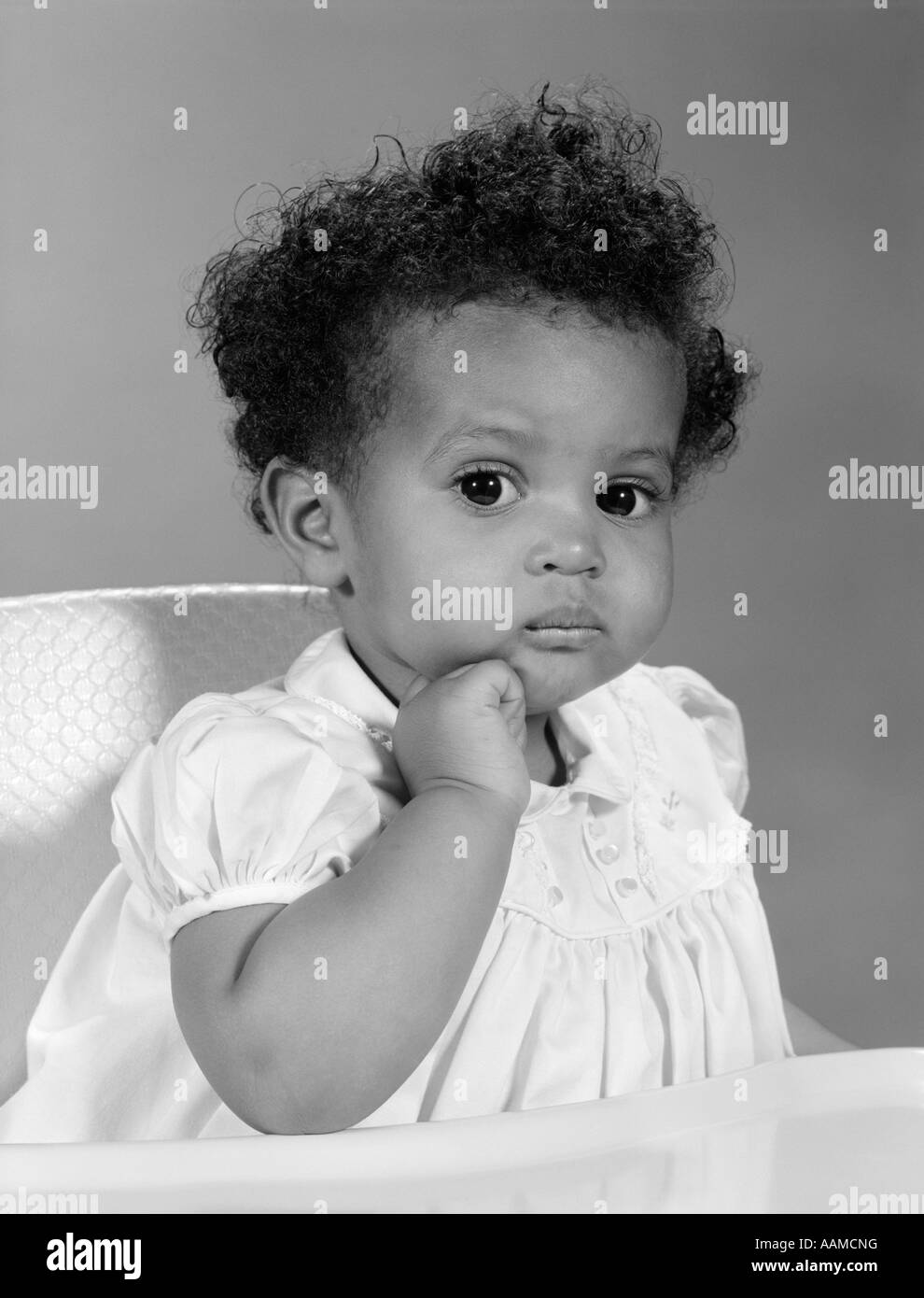 1960s AFRICAN AMERICAN BABY GIRL IN DRESS SITTING IN HIGH CHAIR WITH