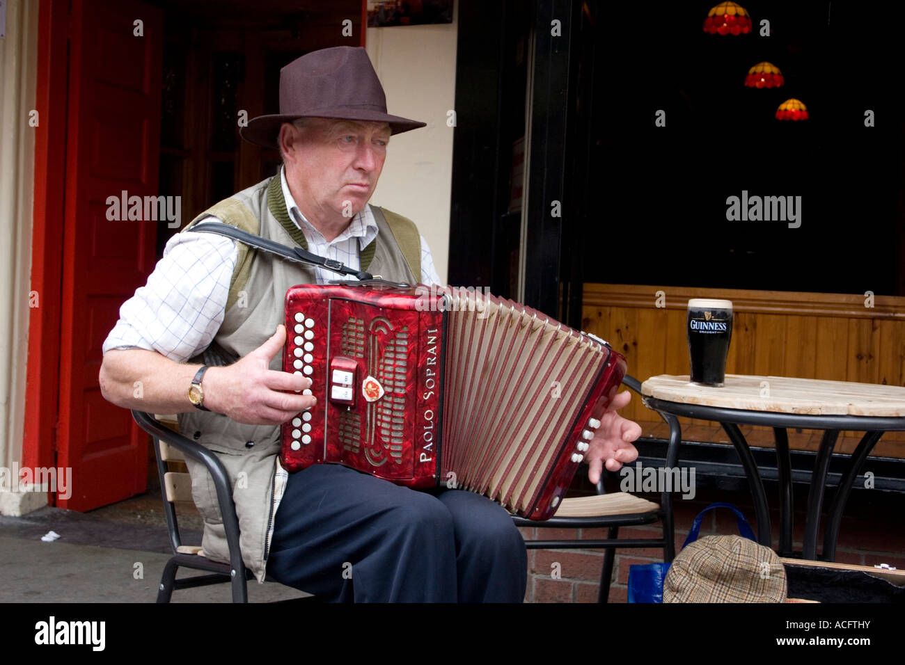 Old Irish man with accordion playing outside pub with glass of Stock