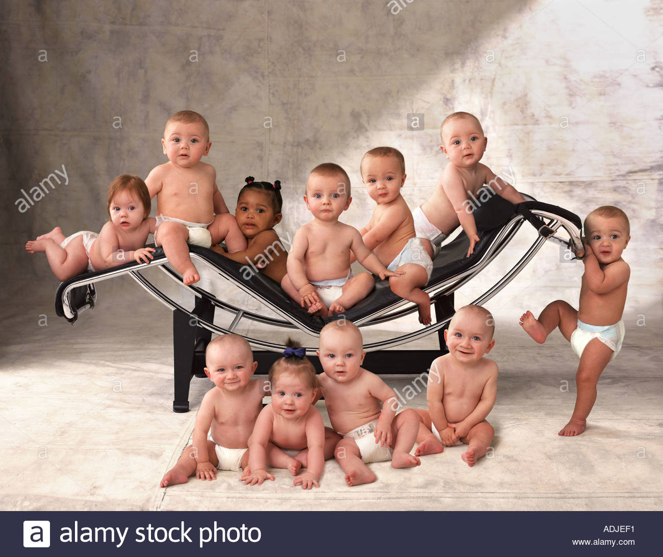A group of eleven babies in daipers sitting on a chaise longue Stock