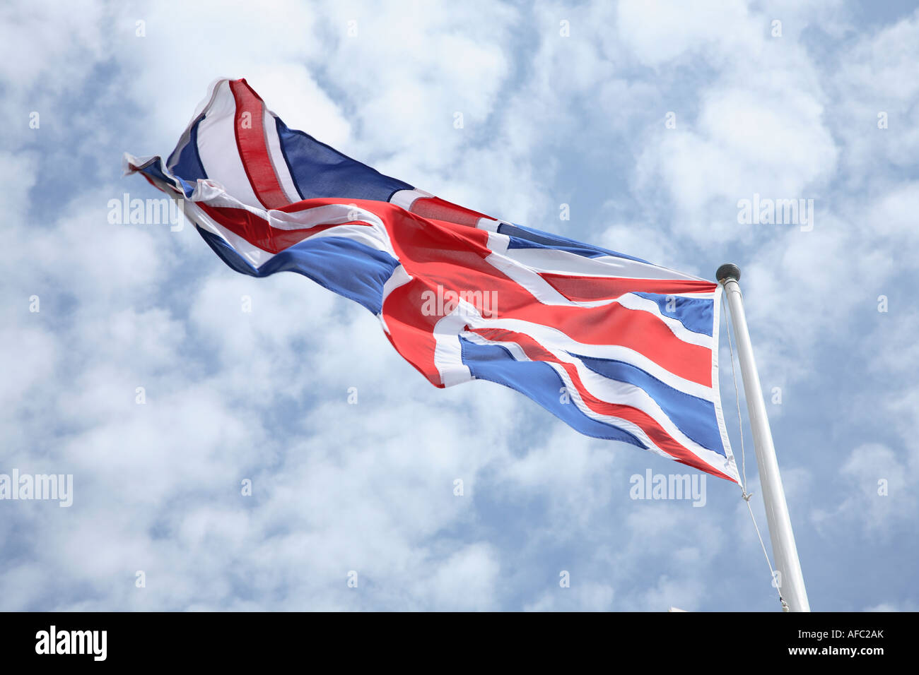 The Union Jack Flag Blowing In The Wind With A Blue Sky And Clouds In