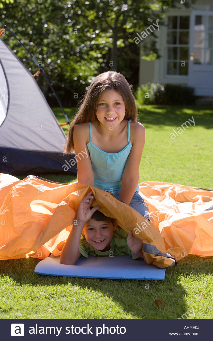 Boy and girl assembling tent in garden girl sitting on top of boy Stock