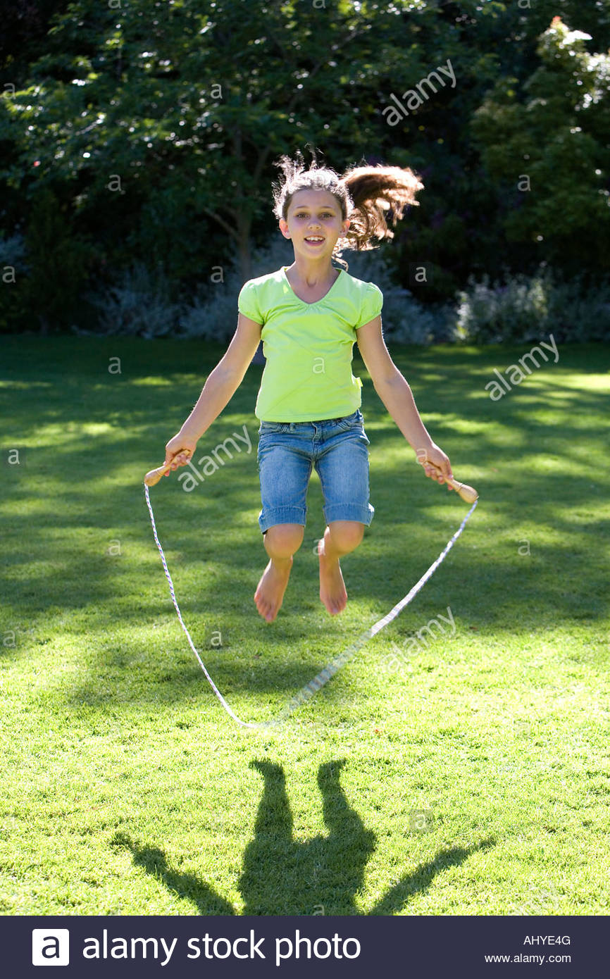 Girl 8 10 playing with skipping rope on garden lawn smiling front Stock