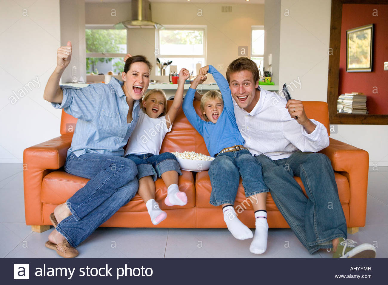 Family of four sitting on sofa in living room, cheering, portrait Stock