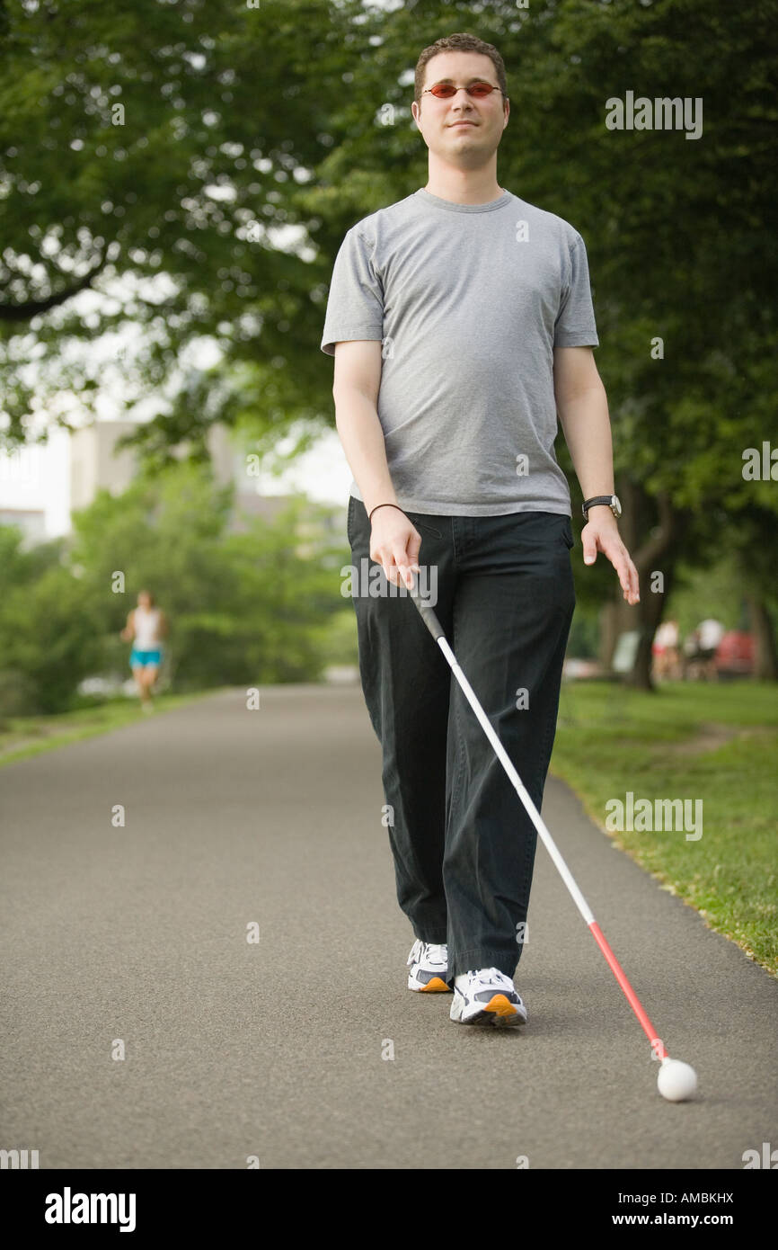 Blind man walking on a walkway with a blind person's cane Stock Photo