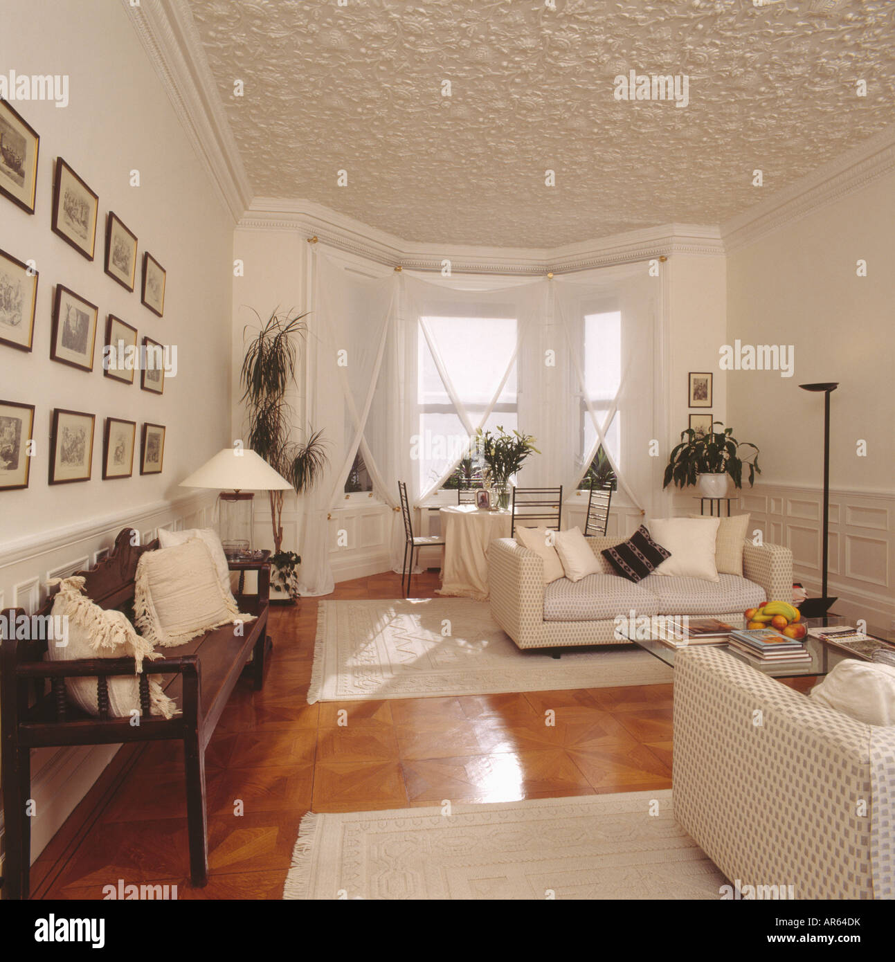 Stock photo textured ceiling in white living room with wooden settle and white sofas cream rugs on polished wooden flooring