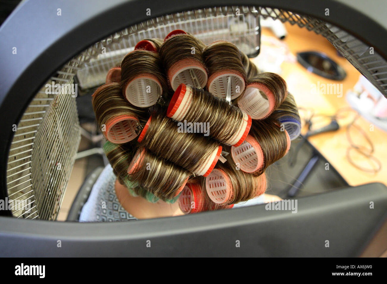close up of a womans head sitting with curlers under hairdryer at Stock