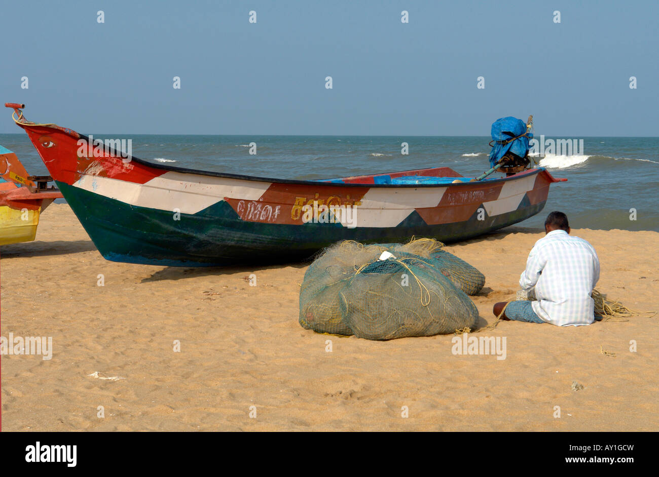 Traditional Indian Fishing Boat And Fisherman Mending Nets On The Beach