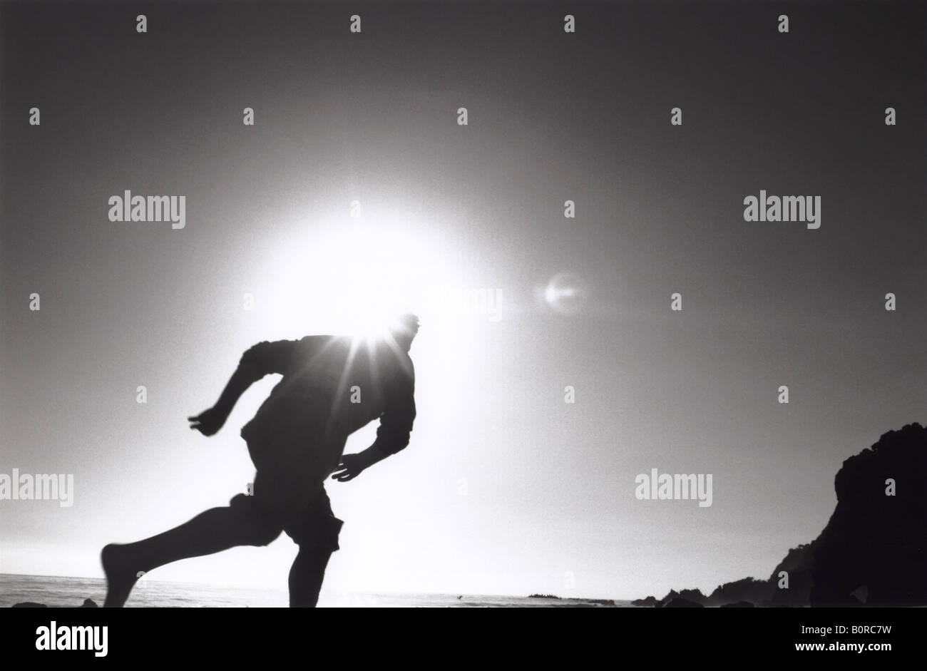 Silhouette Of Man Running On Beach With Sun Behind His Head Flare Glare Blocking Glow Black And White