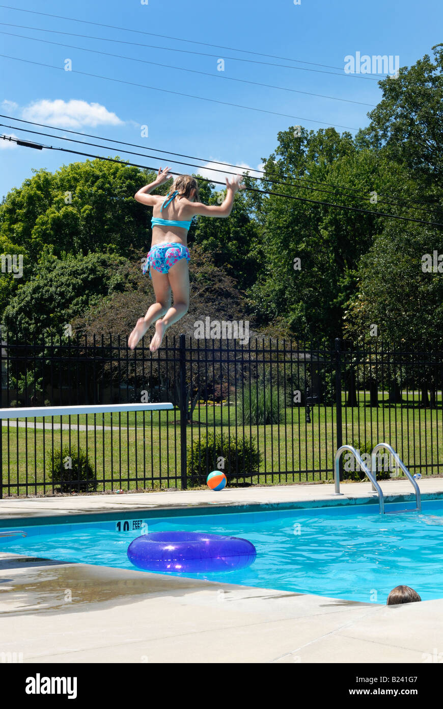 Young girl jumping off a diving board at a neighborhood pool Stock