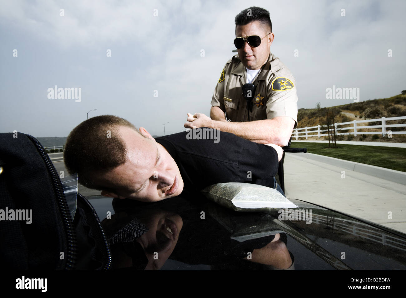 Man being handcuffed by police officer on hood of black