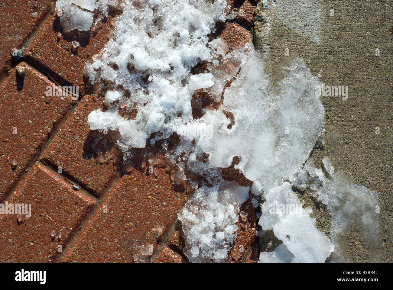 Ice melts along the boundary of concrete and brick sidewalk Stock Photo