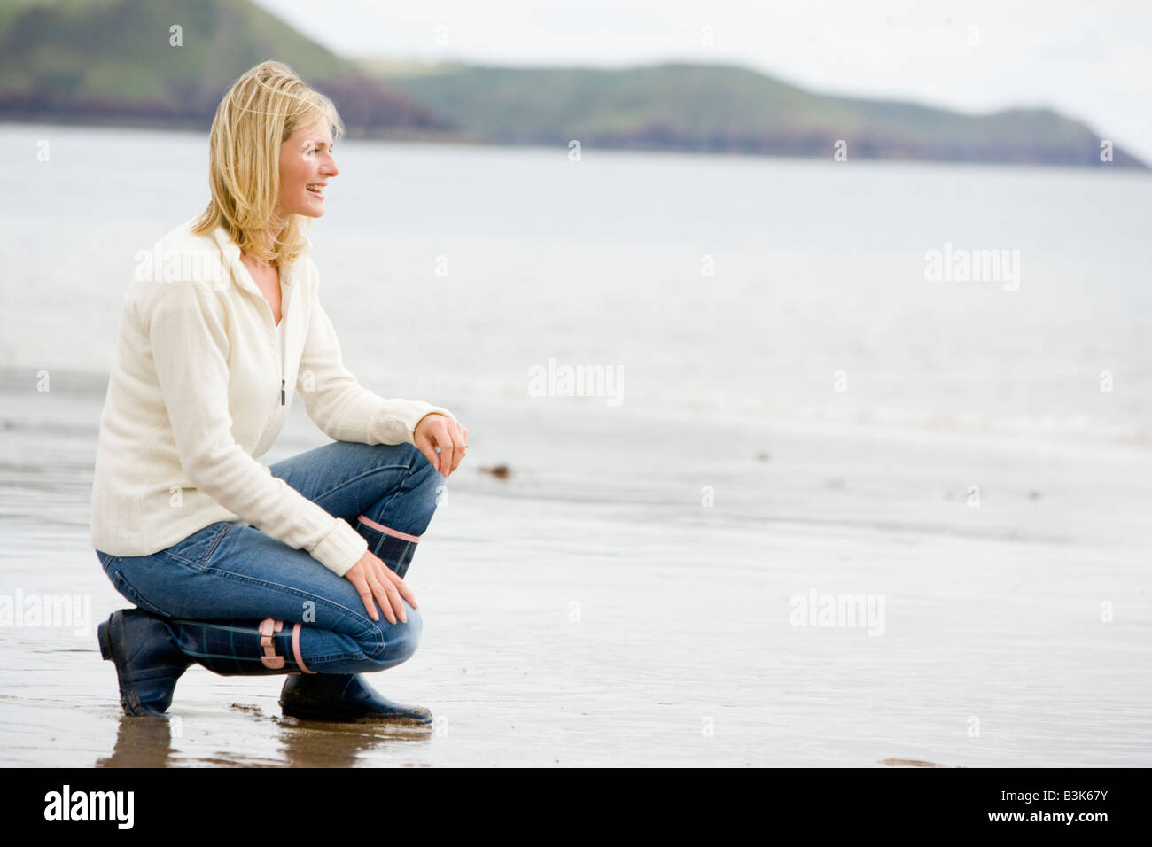 Woman Crouching On Beach Smiling Stock Photo Alamy