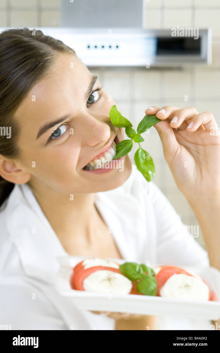 Preview - woman-biting-into-sprig-of-basil-holding-plate-of-caprese-salad-B4A0R2