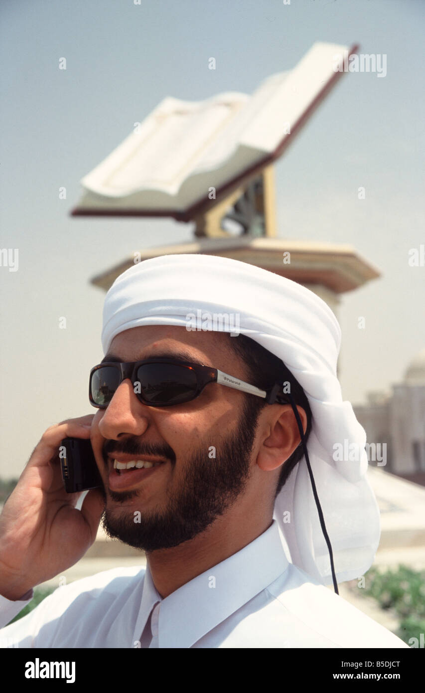 Arab businessman using mobile telephone with kuran koran Qur&#39;ann book statue in background sharjah - arab-businessman-using-mobile-telephone-with-kuran-koran-qurann-book-B5DJCT