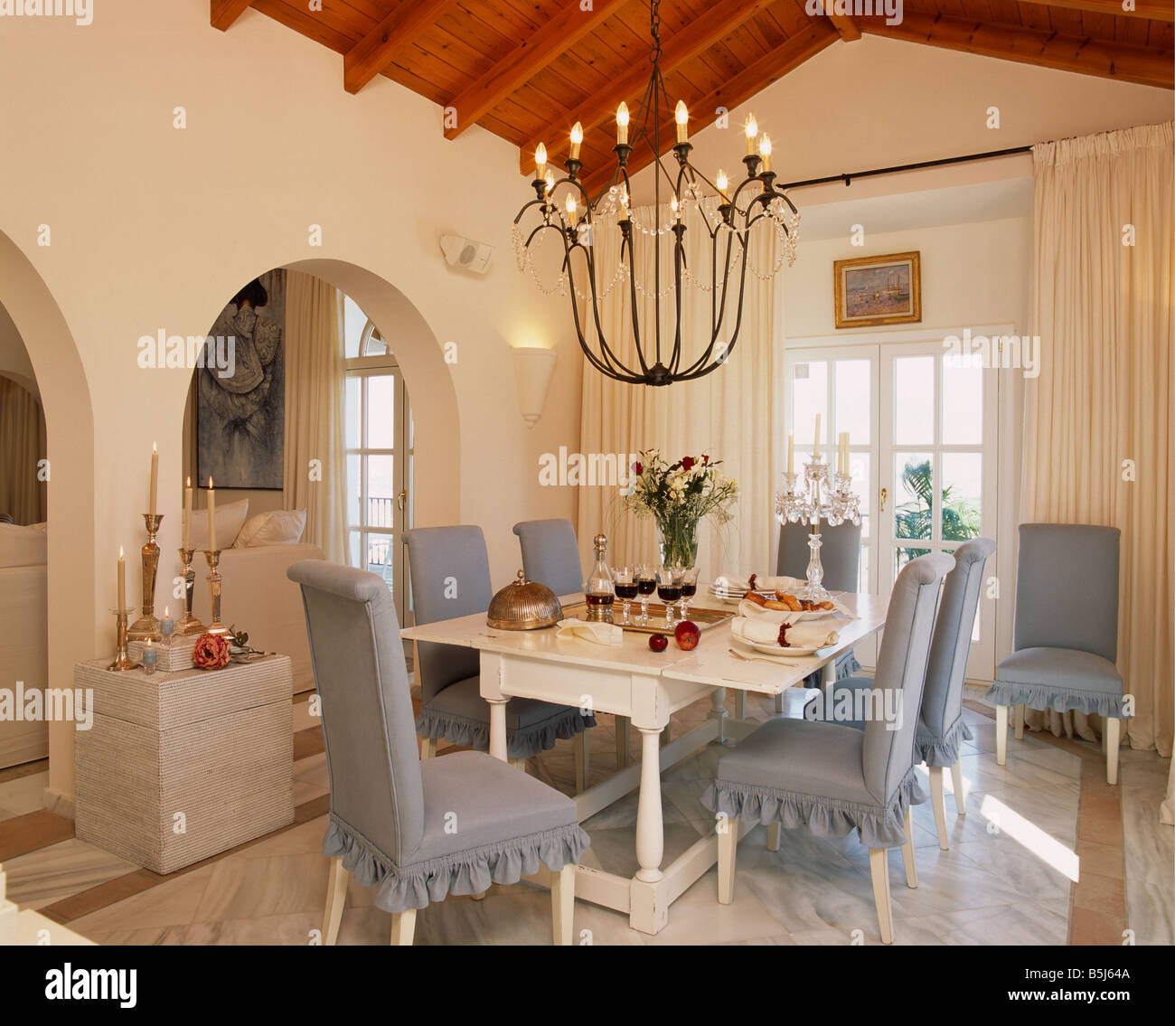 Lighted Metal Chandelier Above White Table And Upholstered Grey