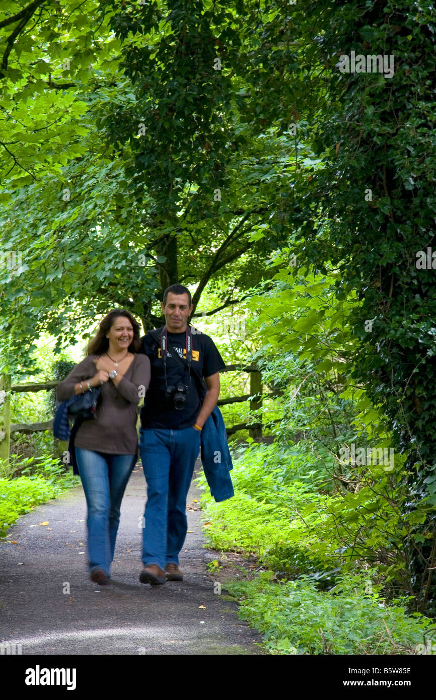 Couple Walking Along A Tree Lined Path In The Village Of Bibury