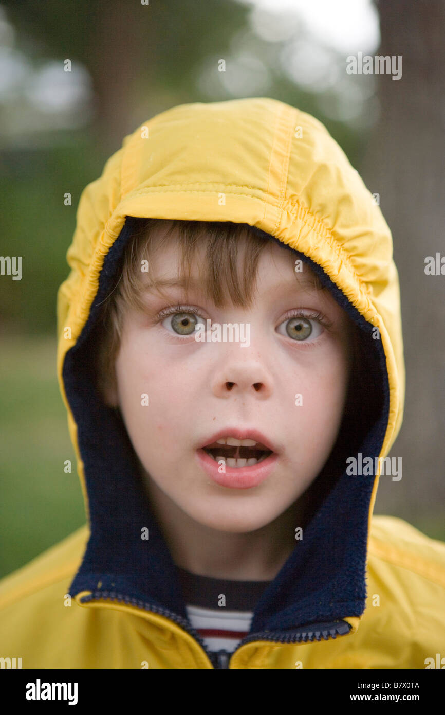 six year old boy wearing a yellow raincoat staring at camera with Stock