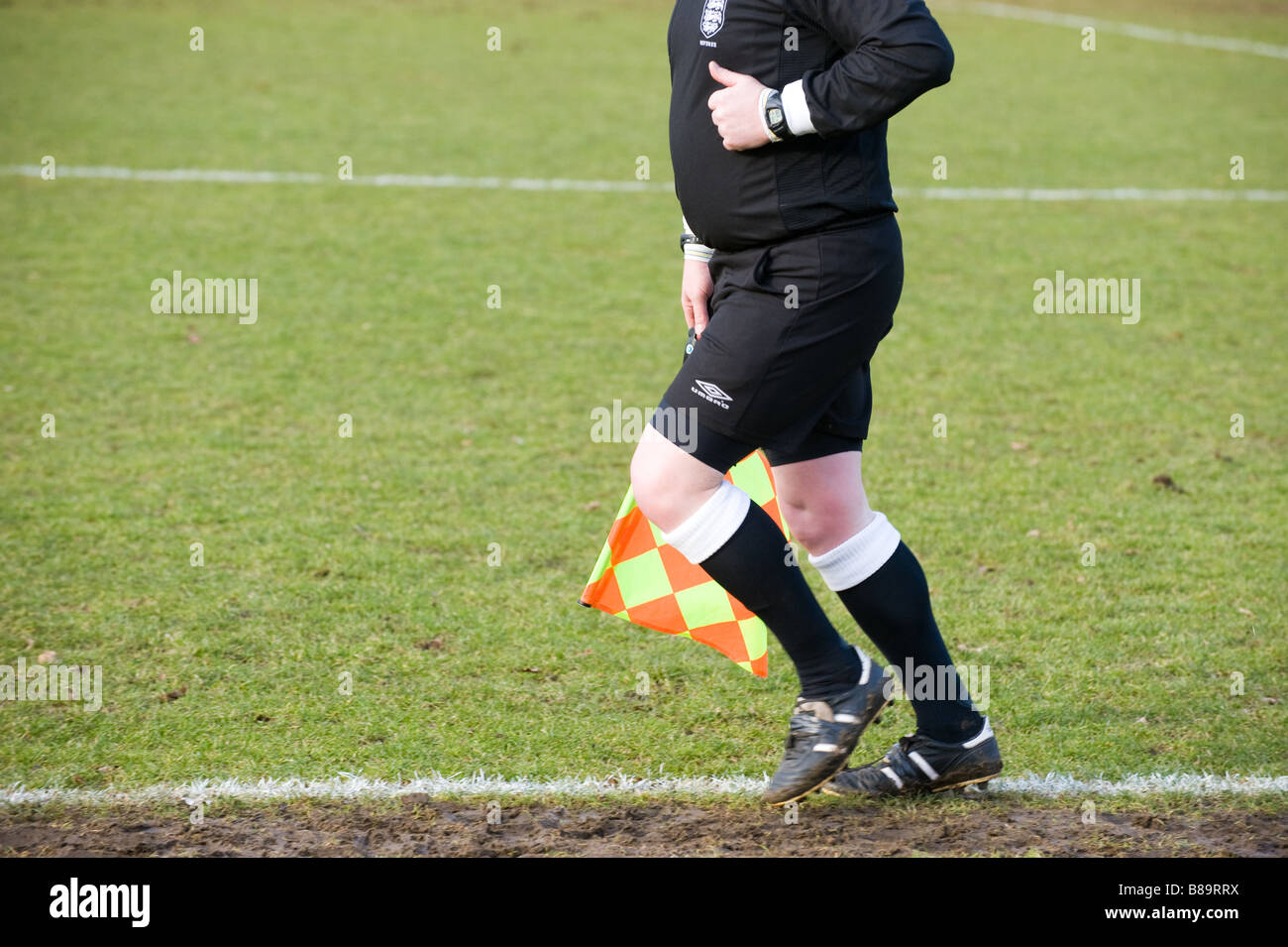Linesman runs along touchline of football pitch Stock Photo, Royalty