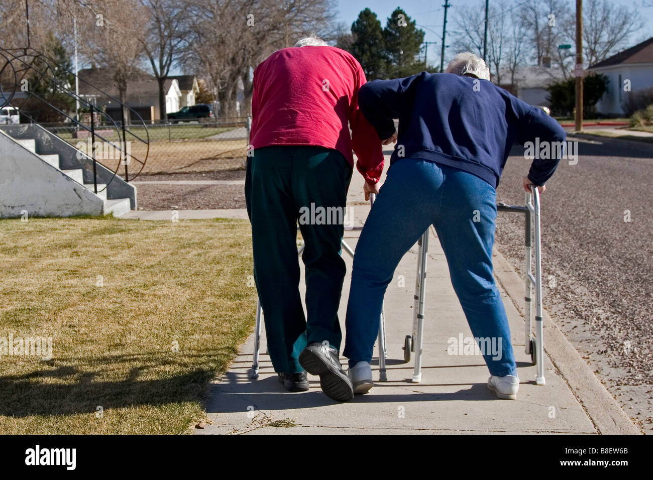 Two elderly senior citizens walk away using walkers, the woman Stock