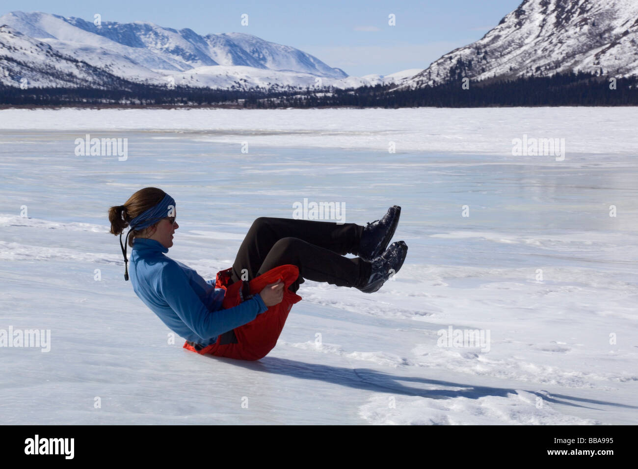 Woman playing, sliding down ice hill on her bottom, overflow Stock