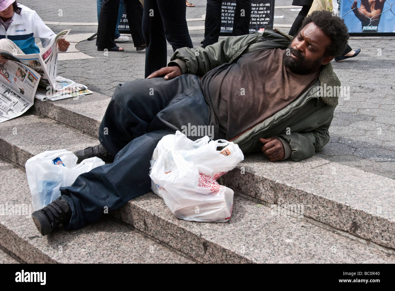 homeless black man in dirty clothing relaxes on the plaza steps in