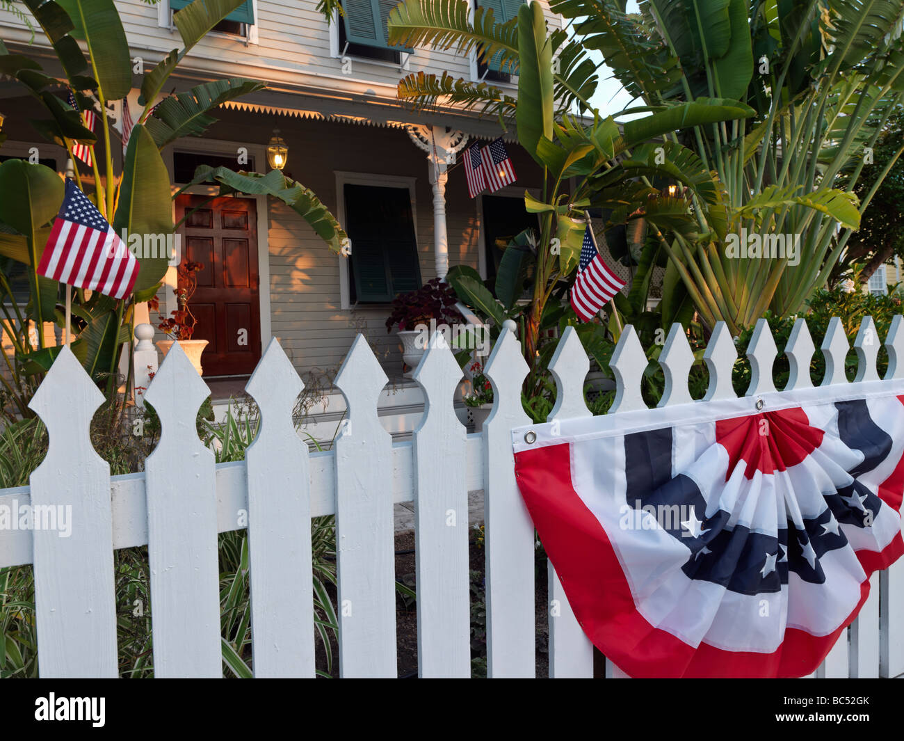 picket fence in front of house with US flags and bunting Stock Photo