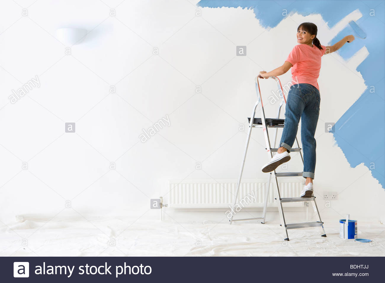 Smiling Woman On Ladder Painting Wall With Paint Roller Smiling Woman On Ladder Painting Wall With Paint Roller